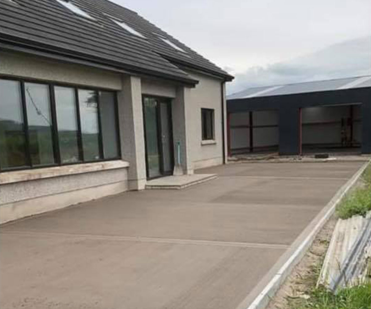 Newly installed smooth concrete driveway in front of a modern home and warehouse