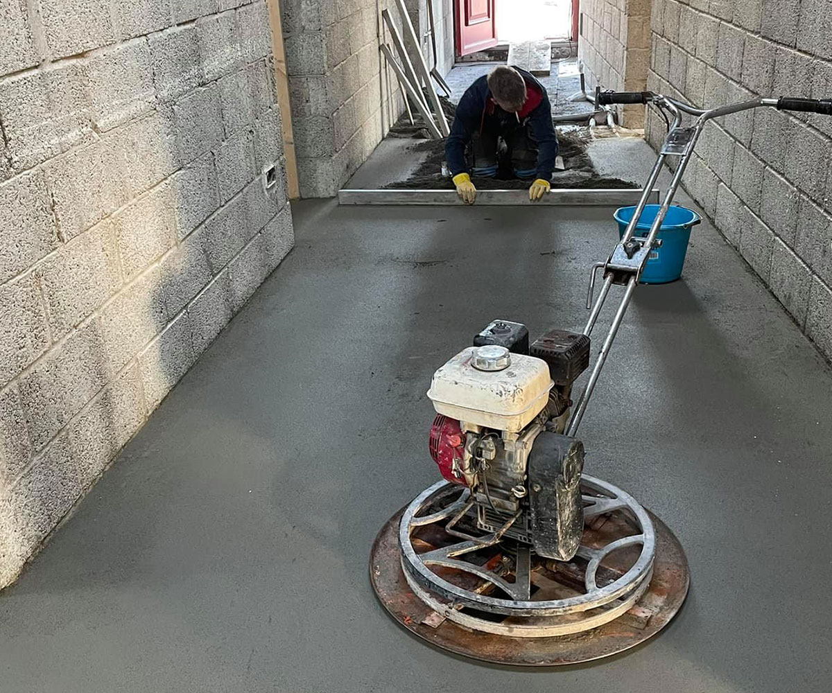 Workers preparing and leveling concrete flooring in a hallway during construction